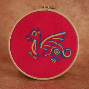 Broderie sur toile rouge d'un petit dragon mignon et naïf coloré dans un style médiéval. Au fil bleu et jaune.