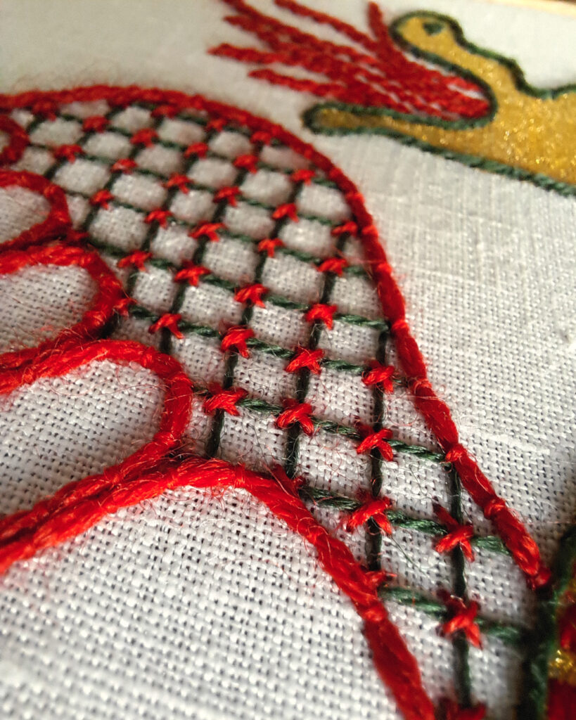 Détail sur la broderie d'une aile de dragon La partie charnue de l'aile est brodée avec un treillis vert foncé avec de petites croix rouges aux intersections.