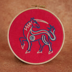 Broderie sur toile rouge : une licorne massive l'air déterminée. Elle est brodée au fil bleu et beige.
