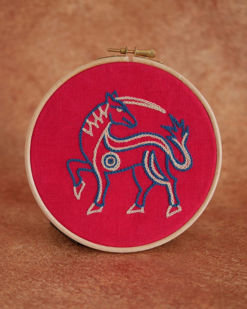 Broderie sur toile rouge : une licorne massive l'air déterminée. Elle est brodée au fil bleu et beige.