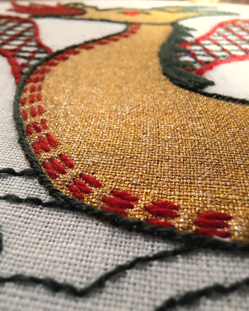 Gros plan sur la broderie du dragon, on voit son corps recouvert d'encre dorée et par dessus, au niveau du ventre, des petits points avant, légèrement espacés brodés en rouge.