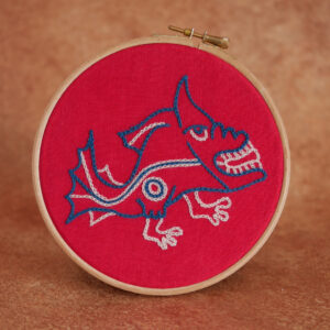 Broderie sur toile rouge et au fil bleu et blanc représentant un poisson mécontent avec des pieds. Ceci dans un style médiéval naïf et bizarre comme ils savaient faire.