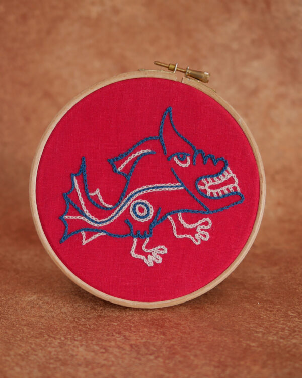 Broderie sur toile rouge et au fil bleu et blanc représentant un poisson mécontent avec des pieds. Ceci dans un style médiéval naïf et bizarre comme ils savaient faire.
