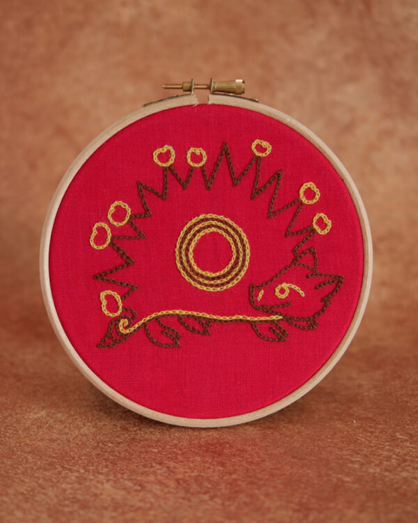 Broderie sur toile rouge : Un hérisson naïf inspiré des enluminures médiévales. Il est marron, de profil avec des fruits jaunes plantés sur ses épines. Il a une tête mignonne, on dirait qu'il sourit et une petite queue en tire-bouchon.