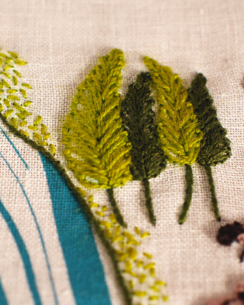 Détail d'une broderie : le long de la côte brodée en vert et vert clair, avec les vagues imprimées, il y a un bosquet de 4 peupliers en vert clair et vert foncé.