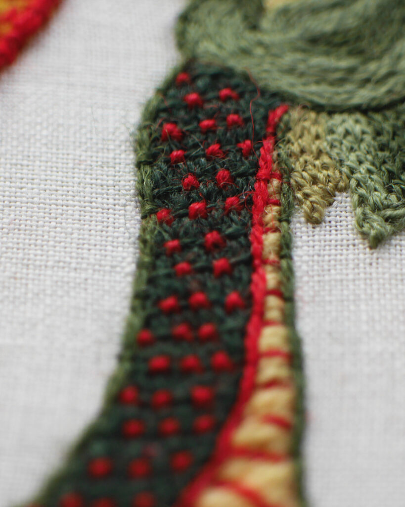 Gros plan sur la broderie du cou et de la tête du dragon. Le contour du cou est brodé avec un fil posé et maintenu par des petits points.