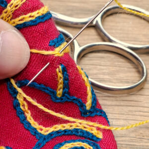 Gros plan sur une broderie avec une aiguille plantée dans le tissu en train de former un point.