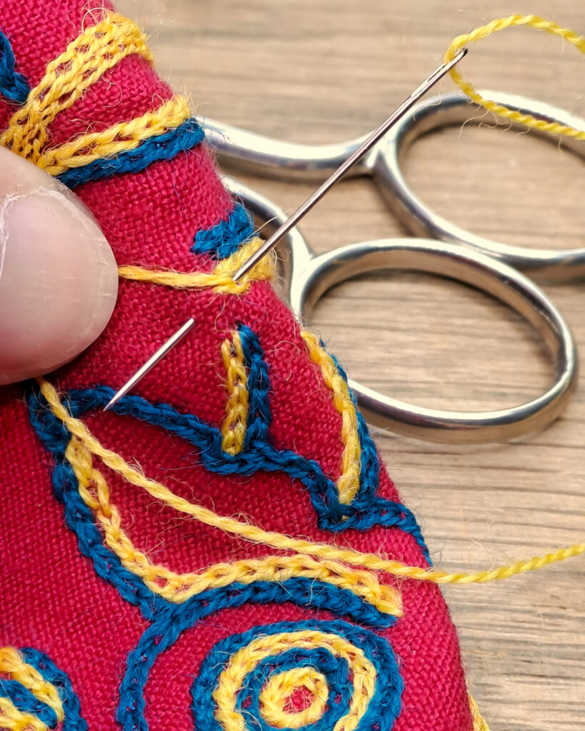 Gros plan sur une broderie avec une aiguille plantée dans le tissu en train de former un point.