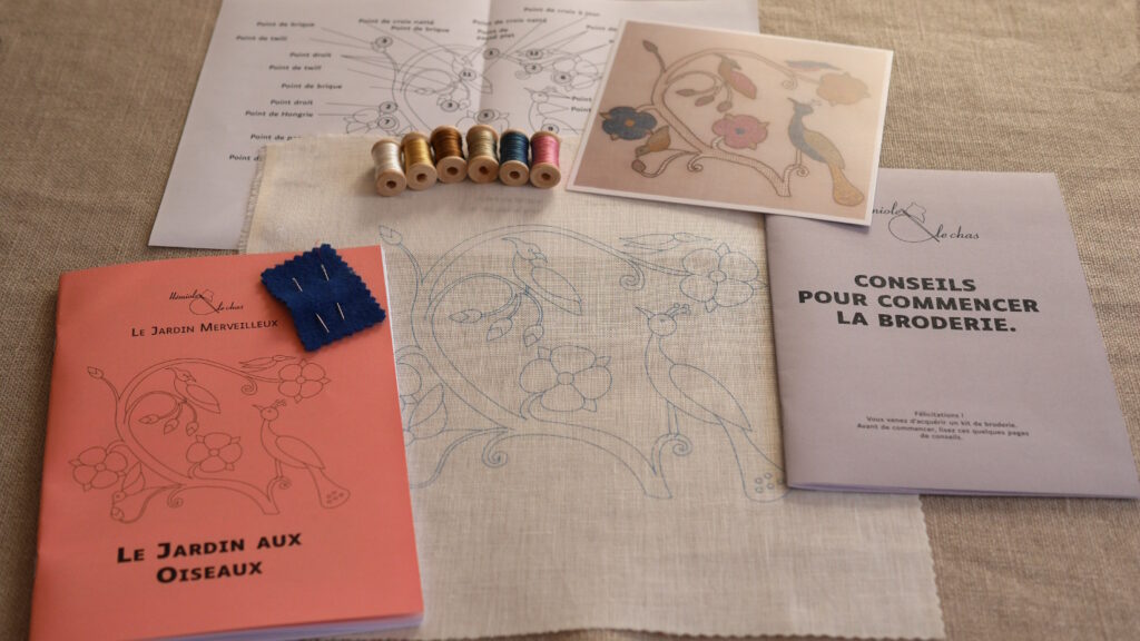 Le contenu d'un kit : la toile blanche avec le motif imprimé, 2 livrets d'explication, 2 aiguilles, 6 bobines de fil, une impression couleur de la broderie terminée et un schéma récapitulatif des points utilisés.