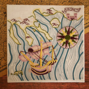 Broderie d'une carte marine les côtes avec des montagnes et du sable, une rose des vents brodée en jaune vert rose et pourpre, un bateau style caravelle brodé en rose jaune et pourpre avec un peu d'écume devant. La mer est imprimée en vagues bleues.