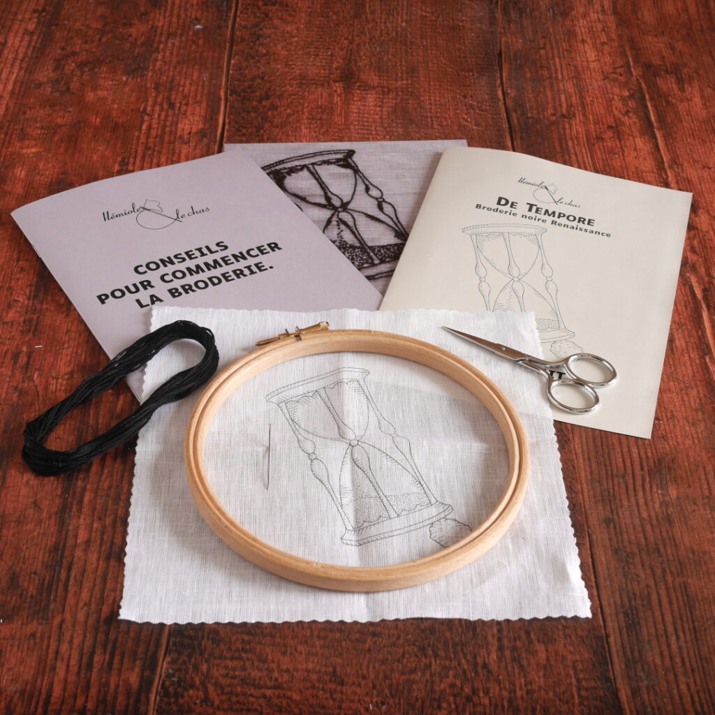 Contenu du kit avec la toile de lin blanche imprimée avec le motif, une échevette de fil noir, une impression couleur de la broderie terminée, 2 livrets de broderie, une aiguille, une paire de petits ciseaux de broderie et un petit tambour de broderie en bois.