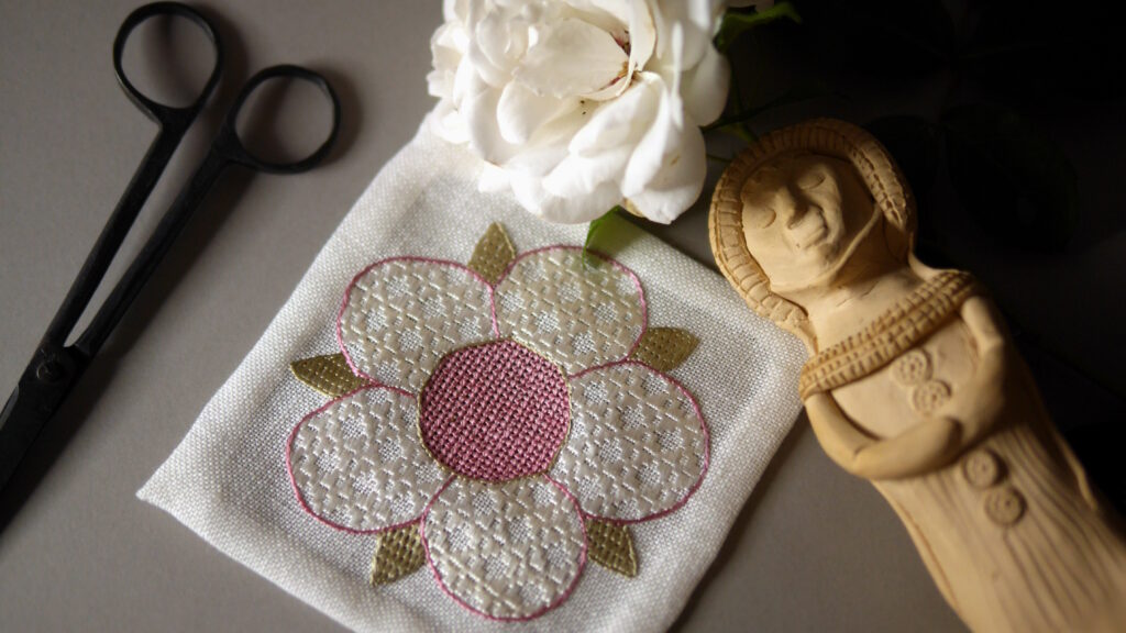Broderie d'une rose médiévale : 5 pétales blancs, un cœur rose pastel et des sépales vert pastel. Tous les remplissages sont réalisés avec des points géométriques qui créent des textures différentes.
