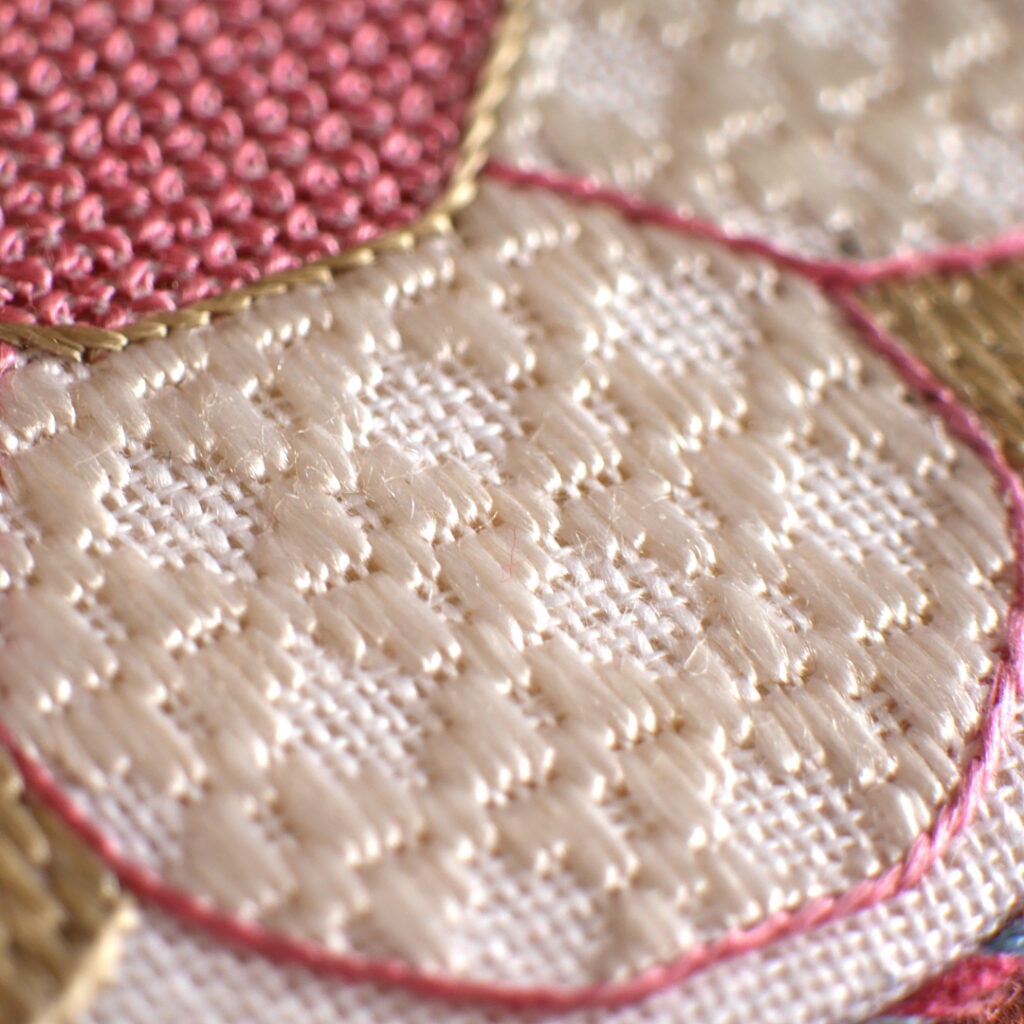 Gros plan sur la broderie de la rose : un pétale avec le contour brodé en rose et rempli au fil blanc qui crée une texture géométrique qui laisse voir la toile blanche en dessous.