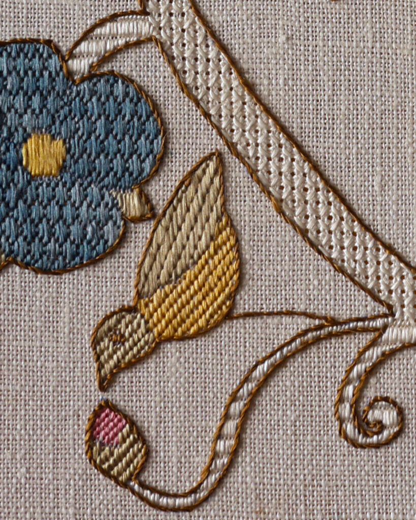 Gros plan sur la broderie du rossignol en jaune et vert, il est penché en avant et picore un bourgeon de rose. On voit aussi une rose brodée en bleu.