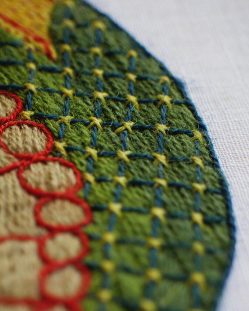 Détail de la broderie du dos du dragon, brodé en 2 nuances de verts moyen et rebrodé d'un treillis vert foncé avec des petites croix jaunes à chaque intersection.