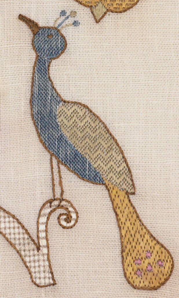 Gros plan sur la broderie du paon en bleu vert et jaune.