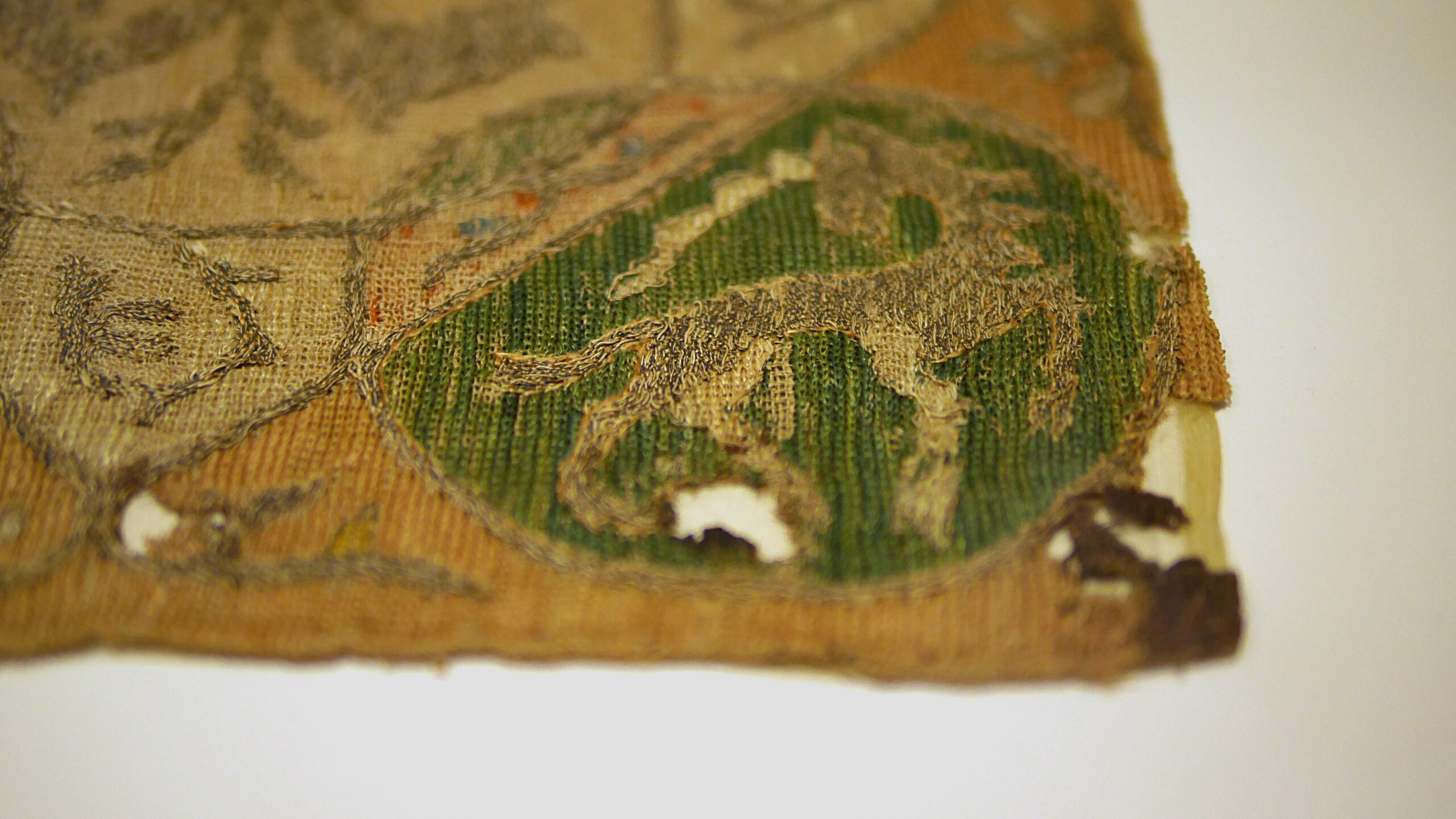 Détail de la broderie d'une aumônière du moyen-âge. On voit un médaillon contenant une licorne brodée au fil d'or. Tout le fond est brodé de points de chaînettes en lignes parallèles collées pour faire le remplissage.