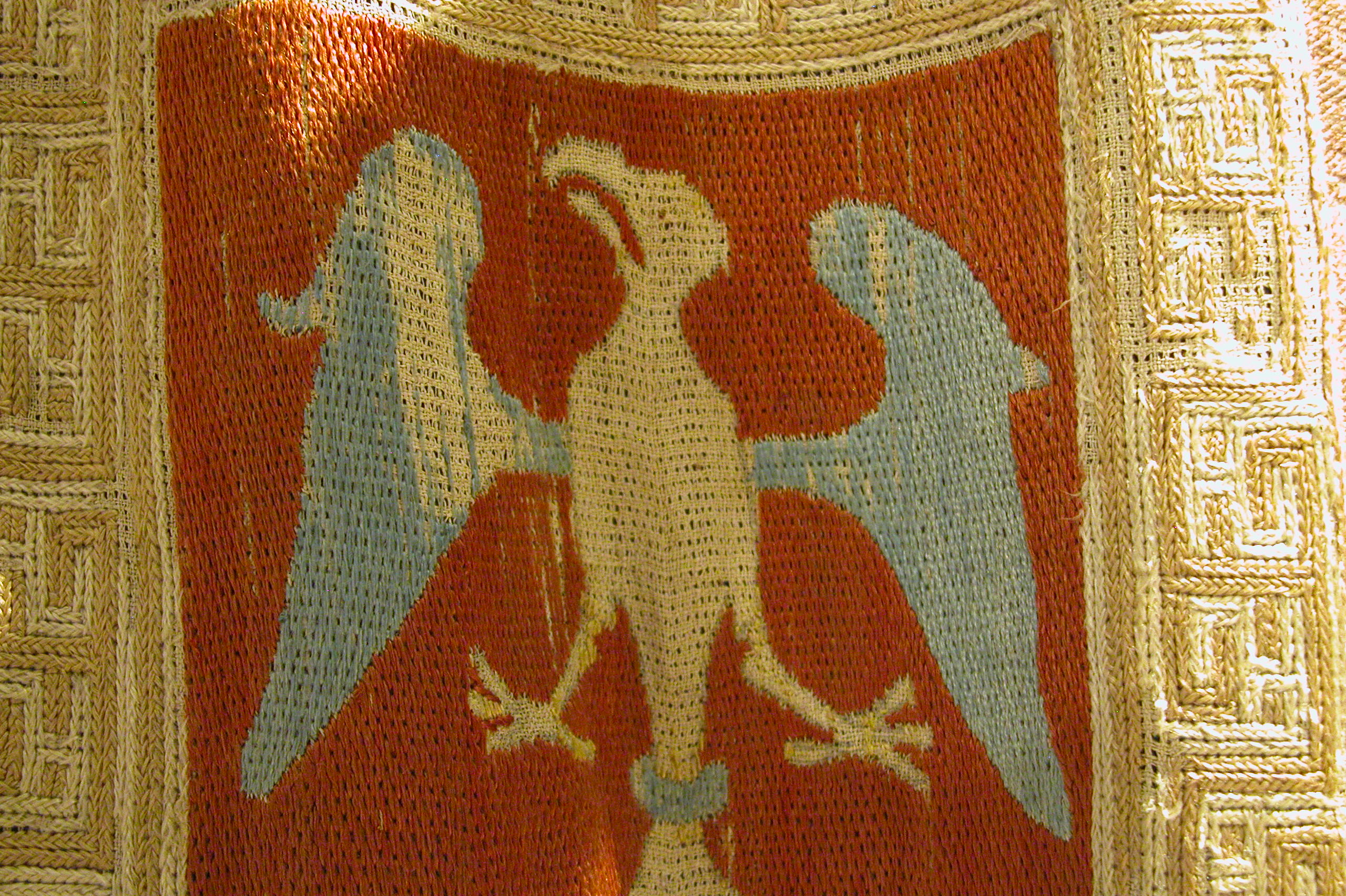 Détail d'une broderie médiévale, un aigle, les ailes écartées brodé au point droit, autour une frise géométrique au point de croix natté.