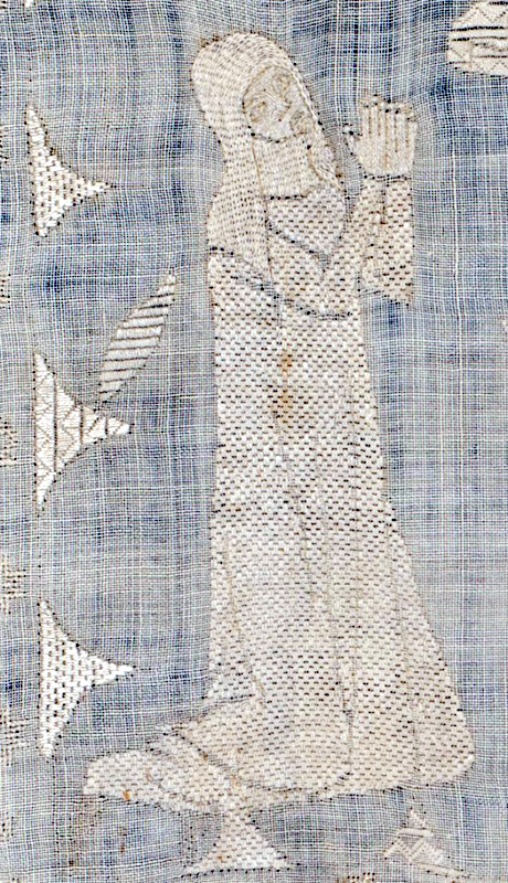 Broderie médiévale au fil blanc sur toile blanche.
Une nonne agenouillée, les mains jointes en position de prière.