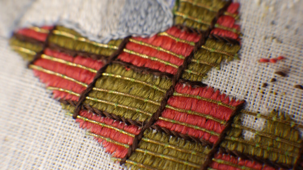 Détail de la broderie de Jutdith : le sol de la tente avec un damier rose et vert sur lequel sont couchés des fils d'or.