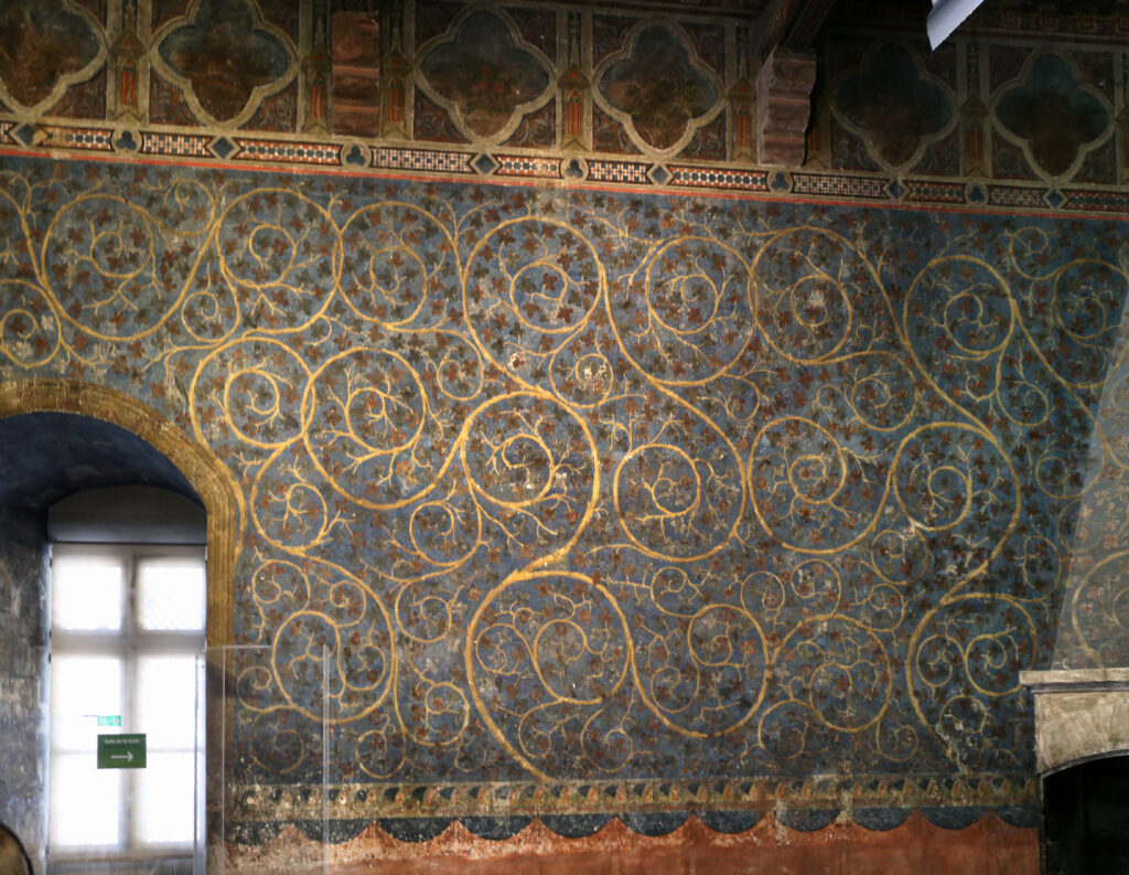 Fresque médiévale murale sur fond bleu foncé, des rinceaux de vigne dorée.