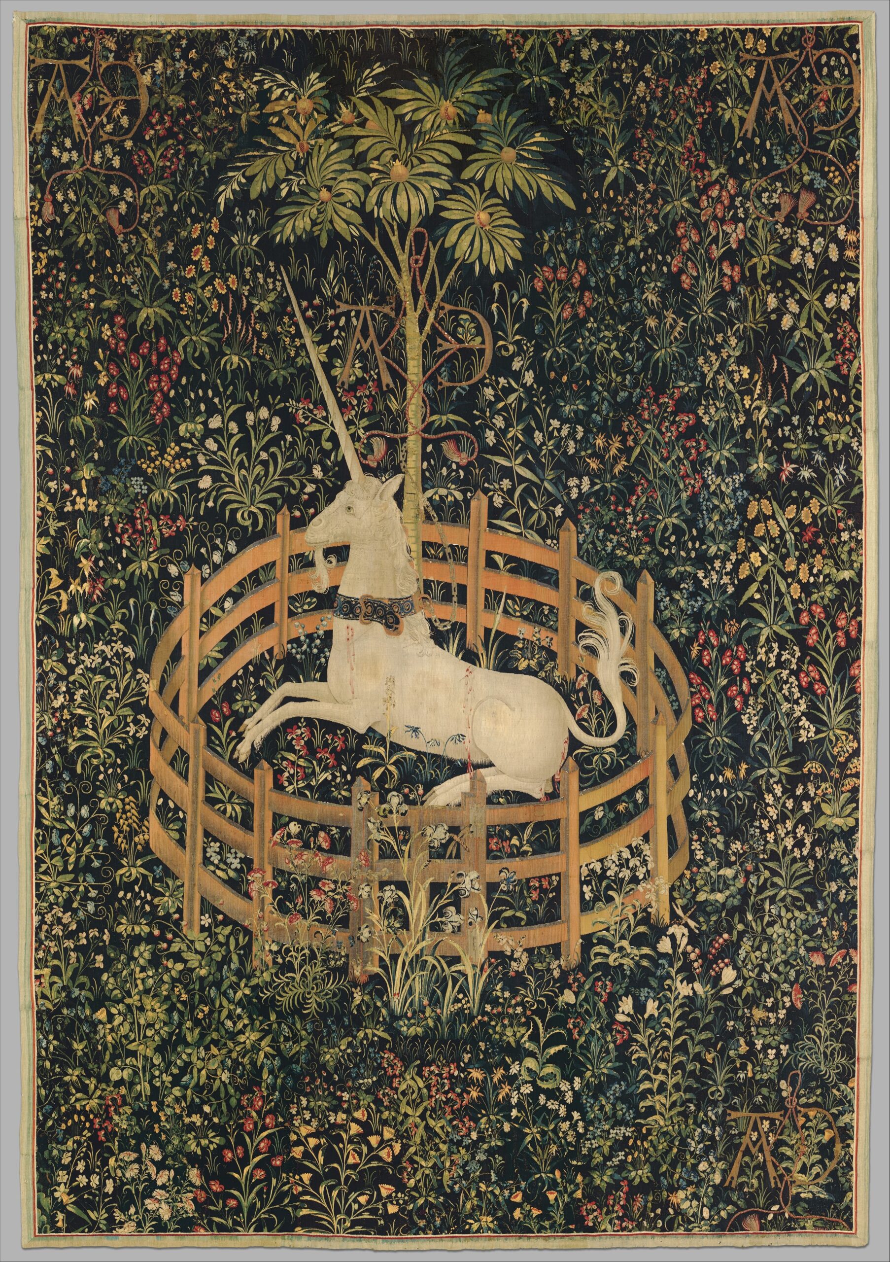 Tapisserie médiévale sur fond vert foncé avec une végétation foisonnante.
Au centre, dans un enclos rond brodé de barrières en bois, il y a une licorne allongée.
Il y a un arbre au milieu.