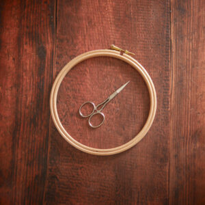 Tambour de broderie en bois clair posé sur une table.