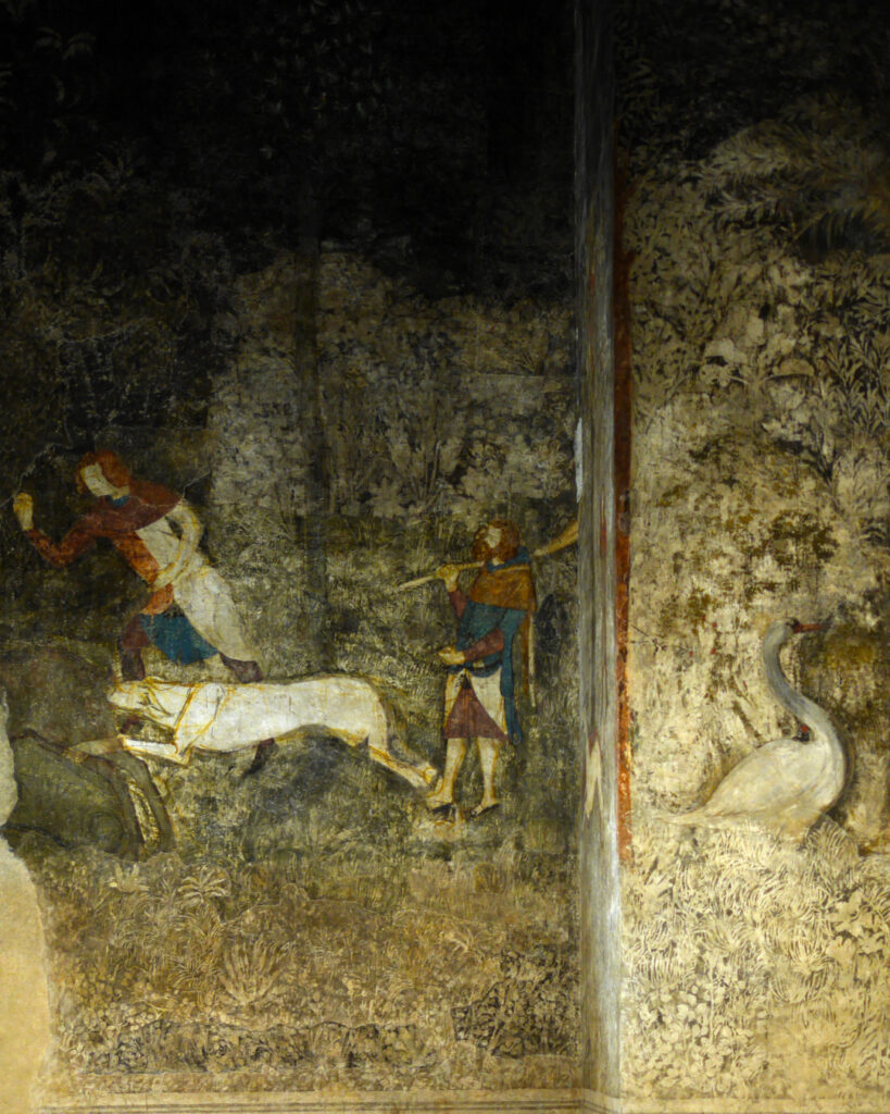 Une fresque médiévale abîmée. Une scène de chasse en forêt avec un fouillis végétal et 2 hommes avec un chien en train de chasser, sur un mur en avant plan, un cygne.
