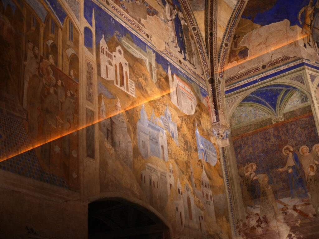 Une fresque médiévale en hauteur. Des paysages de ville avec de la végétation dans des tons assez clairs et un ciel bleu.