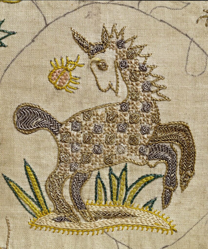 Détail d'une broderie avec des décors végétaux et une licorne. La broderie est réalisée avec des fils colorés et des détails dans la licorne sont brodés au fil d'or.
