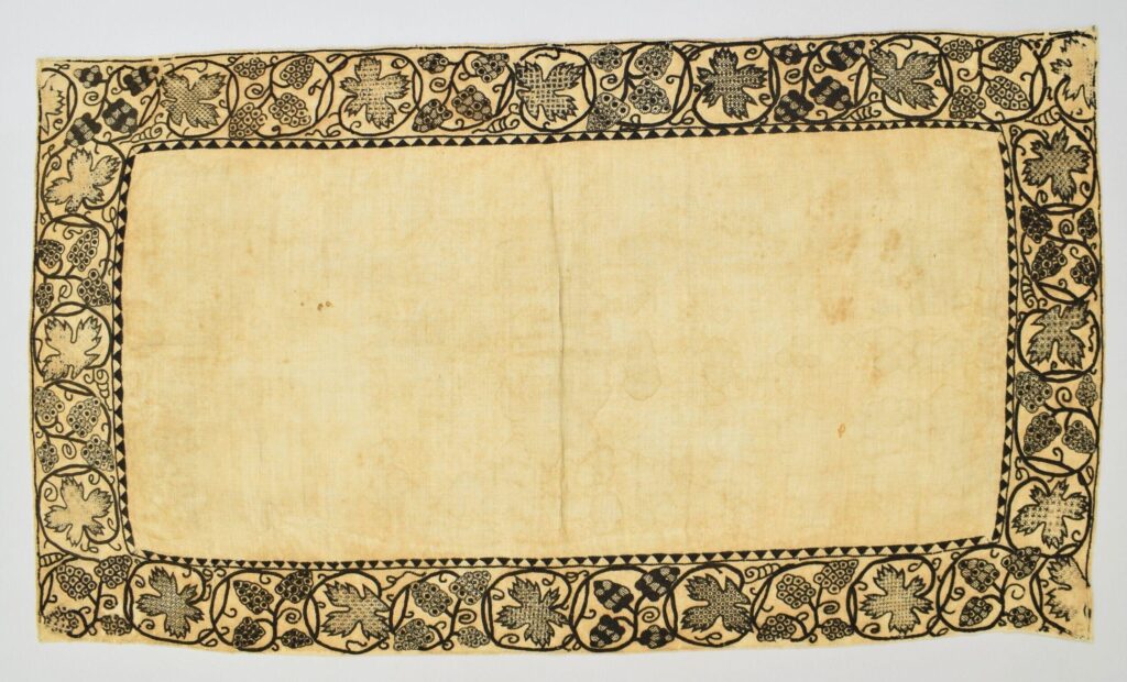 Broderie noire sur toile écrue : la broderie est une frise végétale sur le contour d'une pièce rectangulaire. Le remplissage des feuilles et fleurs est brodé avec des points géométriques.