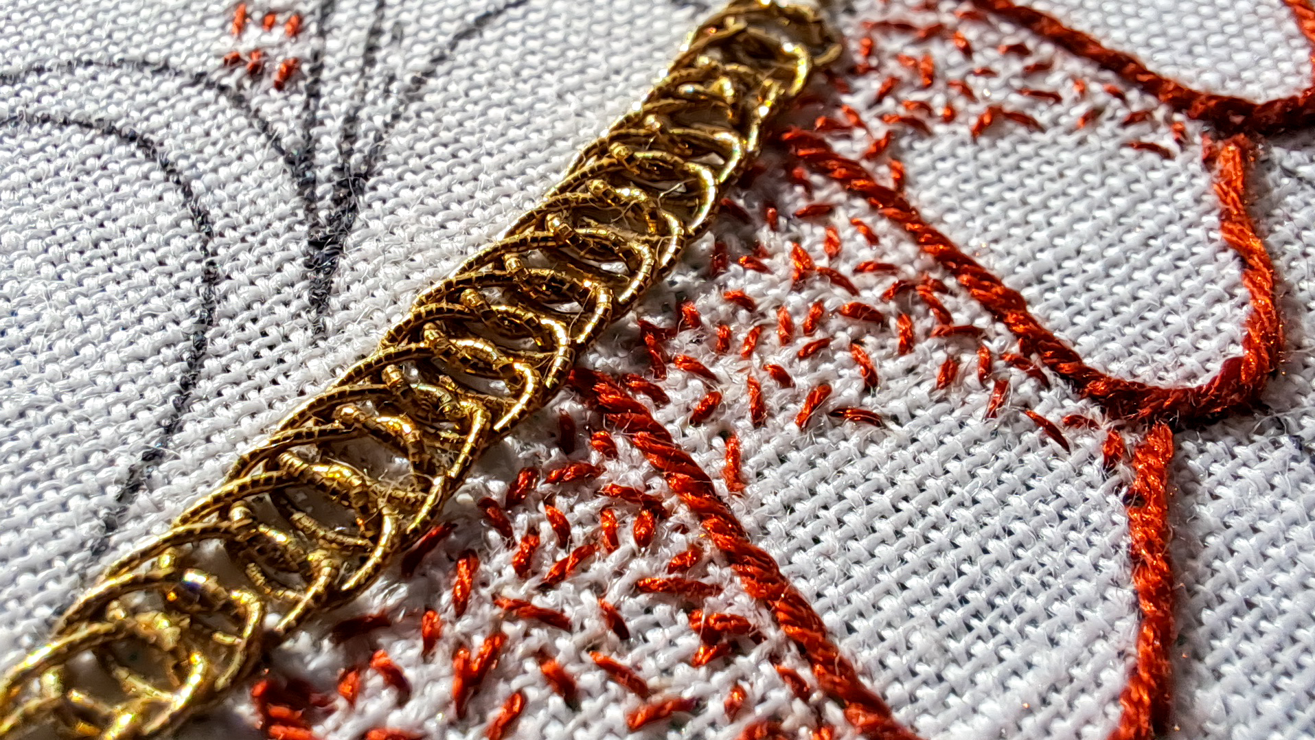 Très gros plan sur une broderie sur toile blanche, avec du fil rouge et une ligne tressée au fil d'or au centre.